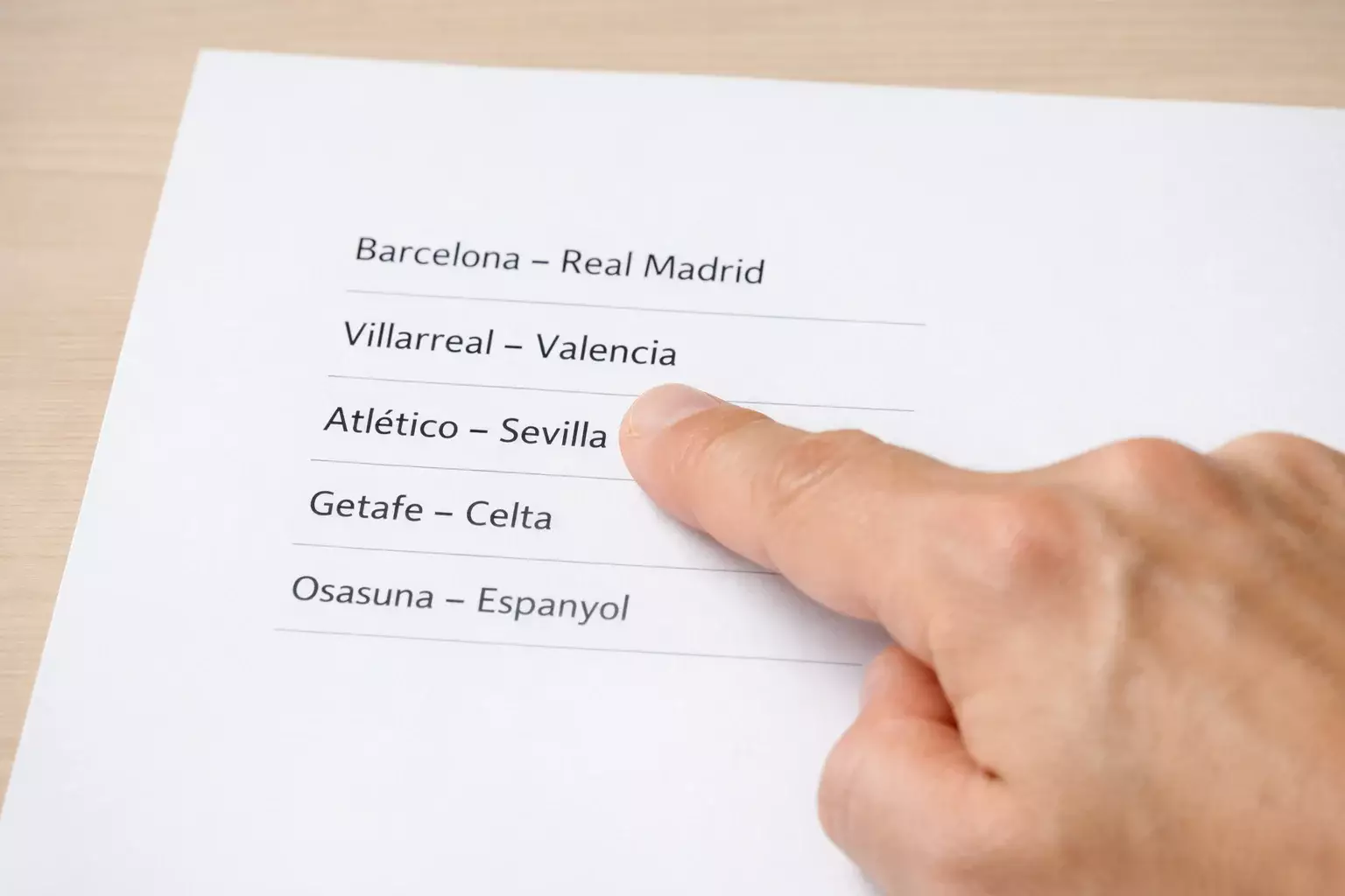 Mano señalando una única opción en una lista de partidos de fútbol